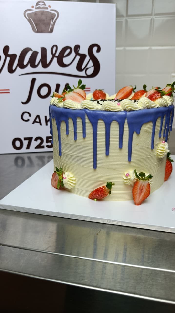 Cake with a coloured drip, piped cream swirls and fresh strawberries on top.